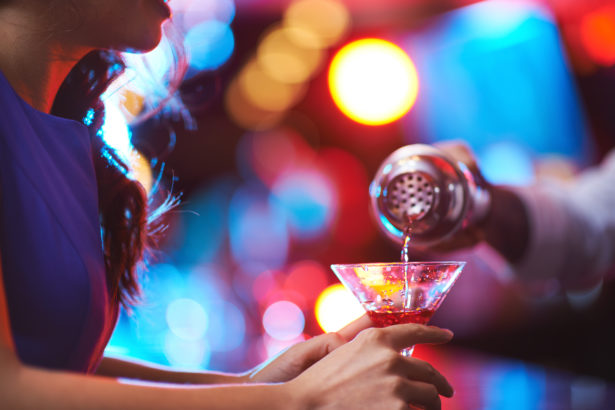 Young girl holding martini glass with red drink in the bar