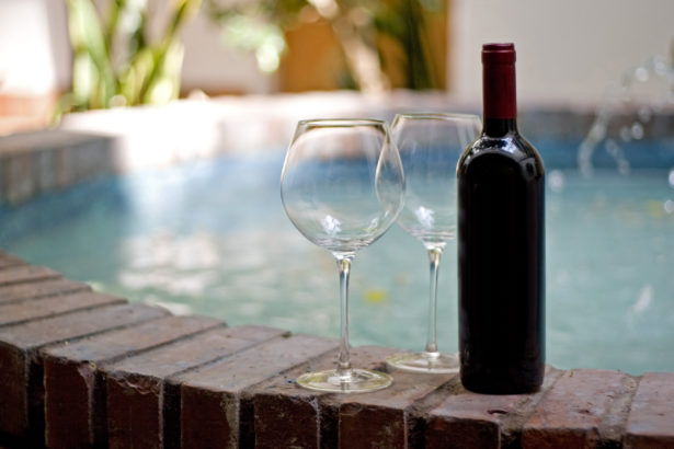 A red wine bottle and two empty glasses by the pool.