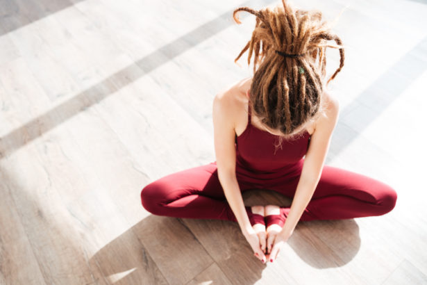 Modern young woman with dreadlocks sitting and doing yoga