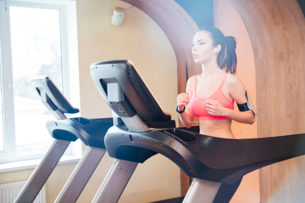 Pretty focused young woman athlete running on treadmill in gym